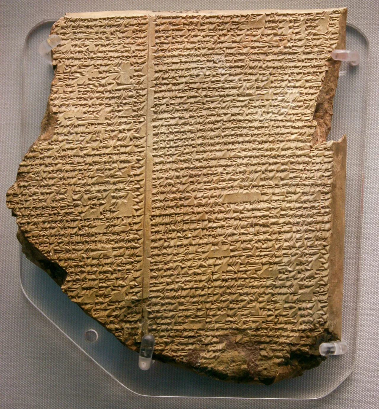 The broken clay Flood Tablet, with dense columns of cuneiform and damaged edges, displayed on a grey support.