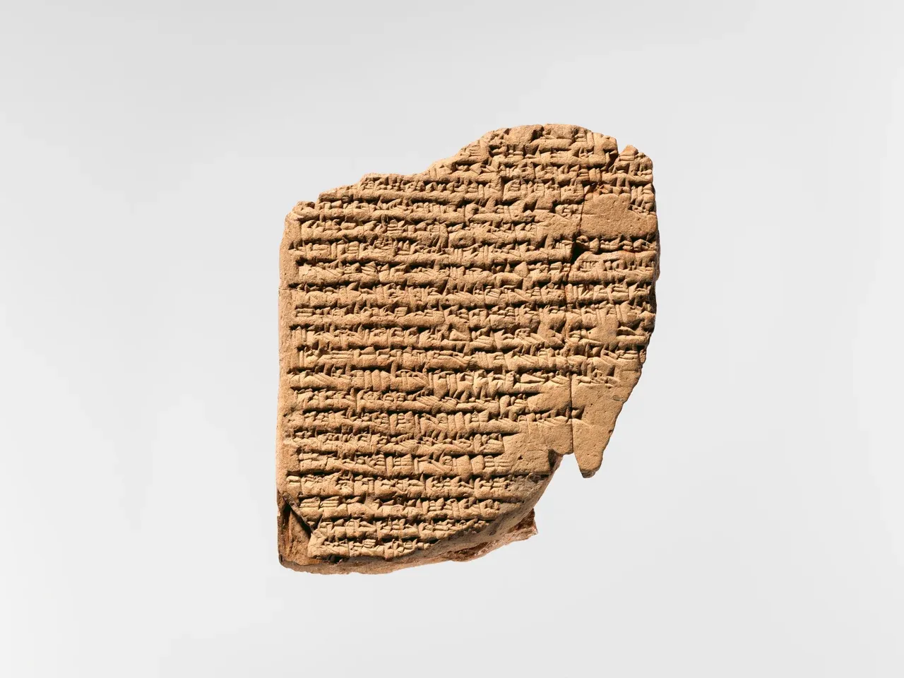 A broken brown clay tablet covered with dense rows of cuneiform, with missing areas along its edges.