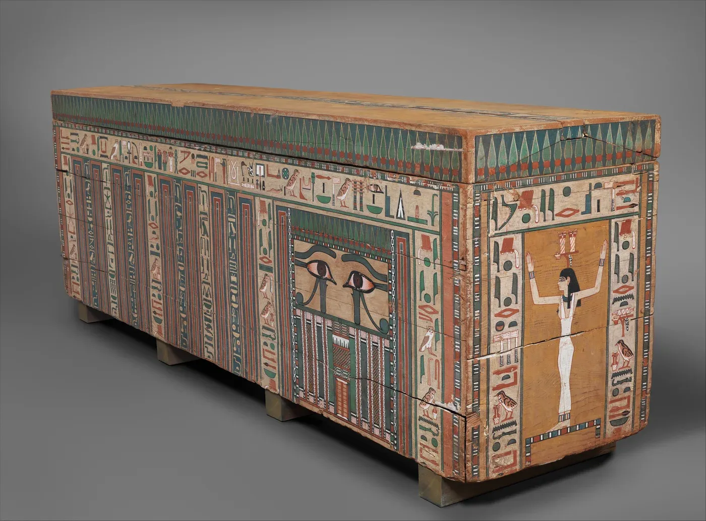 A rectangular wooden coffin covered in painted hieroglyphs and coloured panels, with a pair of eyes above a false door on its long side.