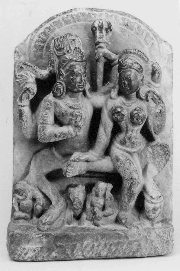 An old black-and-white photograph of a small stone relief with an arched top. A god and a goddess sit side by side, his arm around her, with a staff rising between them; small figures and an animal crouch at their feet.