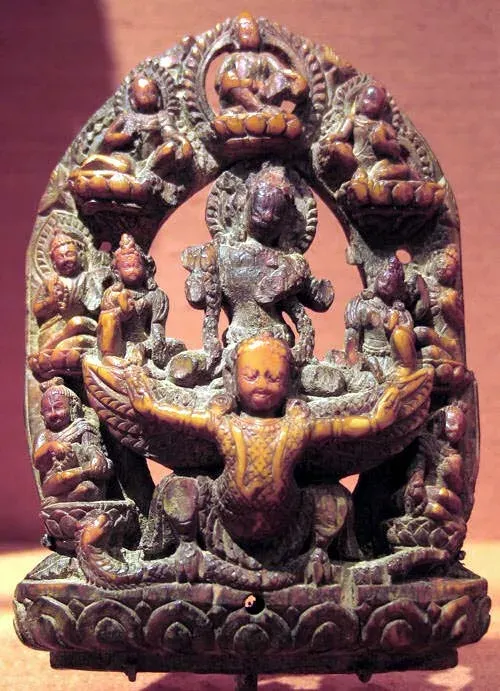 An ivory plaque with an arched top, densely carved. In the centre a winged figure with outstretched arms carries a seated god on his shoulders; smaller seated figures are set on lotuses around the arch and at the sides.