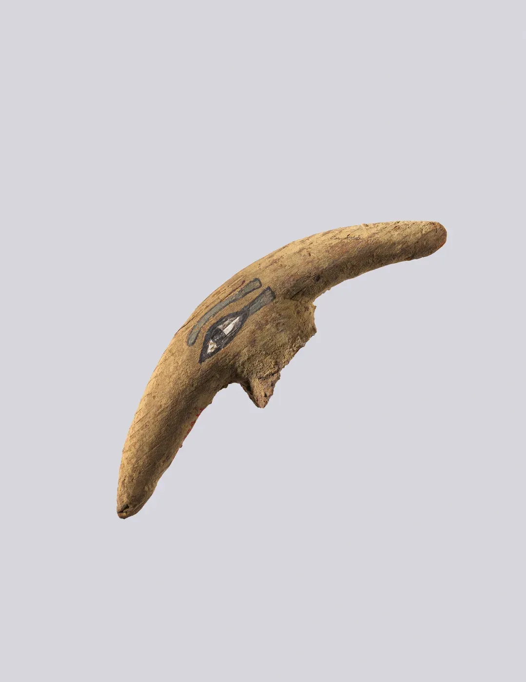 A curved, horn-like piece of yellowish wood with a broken projection on its lower edge. A human eye with a long cosmetic line and an eyebrow is painted on its side in black, white and grey-green.